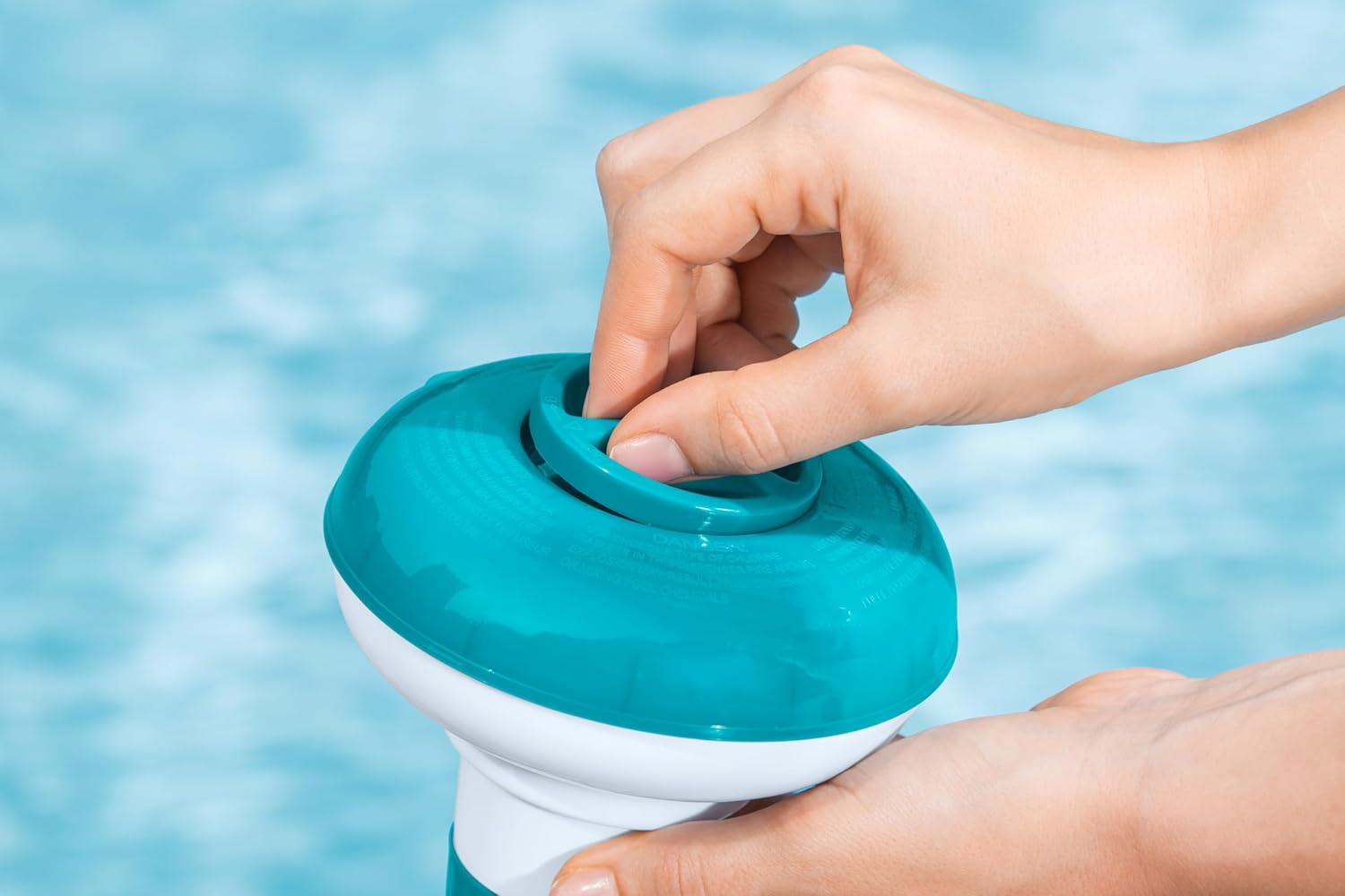 Eine Hand dreht eine weiße und türkise Pool-Chemikalien-Spenderkappe.