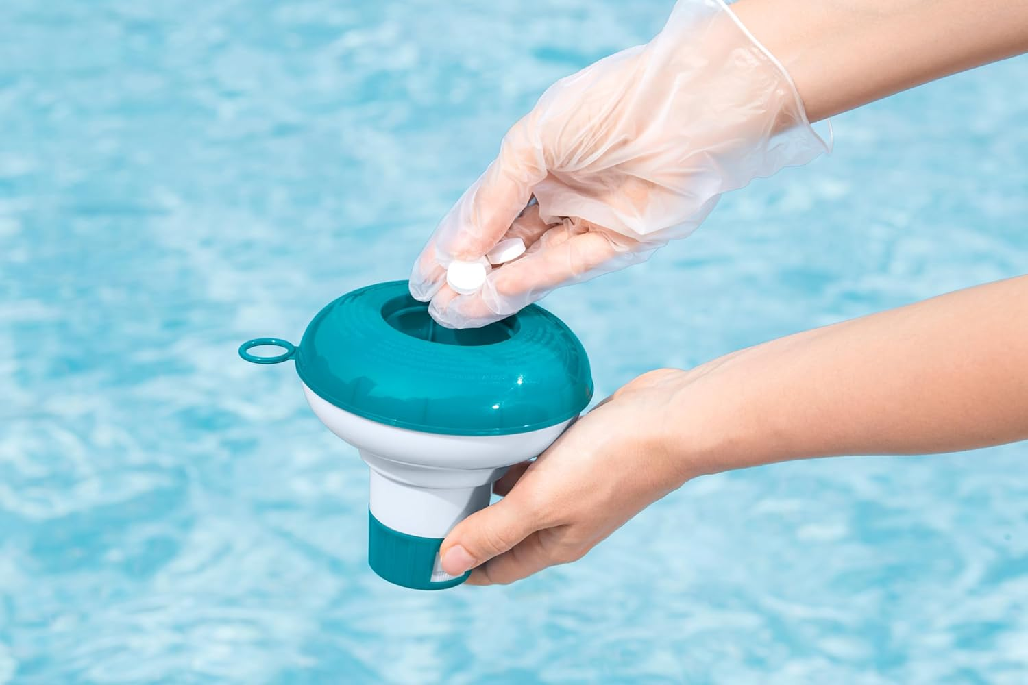 Eine Hand mit Handschuh legt Tabletten in einen blauen und weißen Pool-Schwimmer.