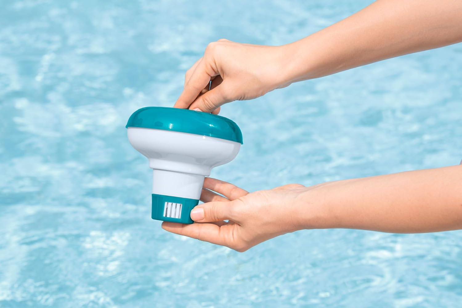 Hände halten einen blauen und weißen Pool-Chemikalien-Spender über blauem Wasser.