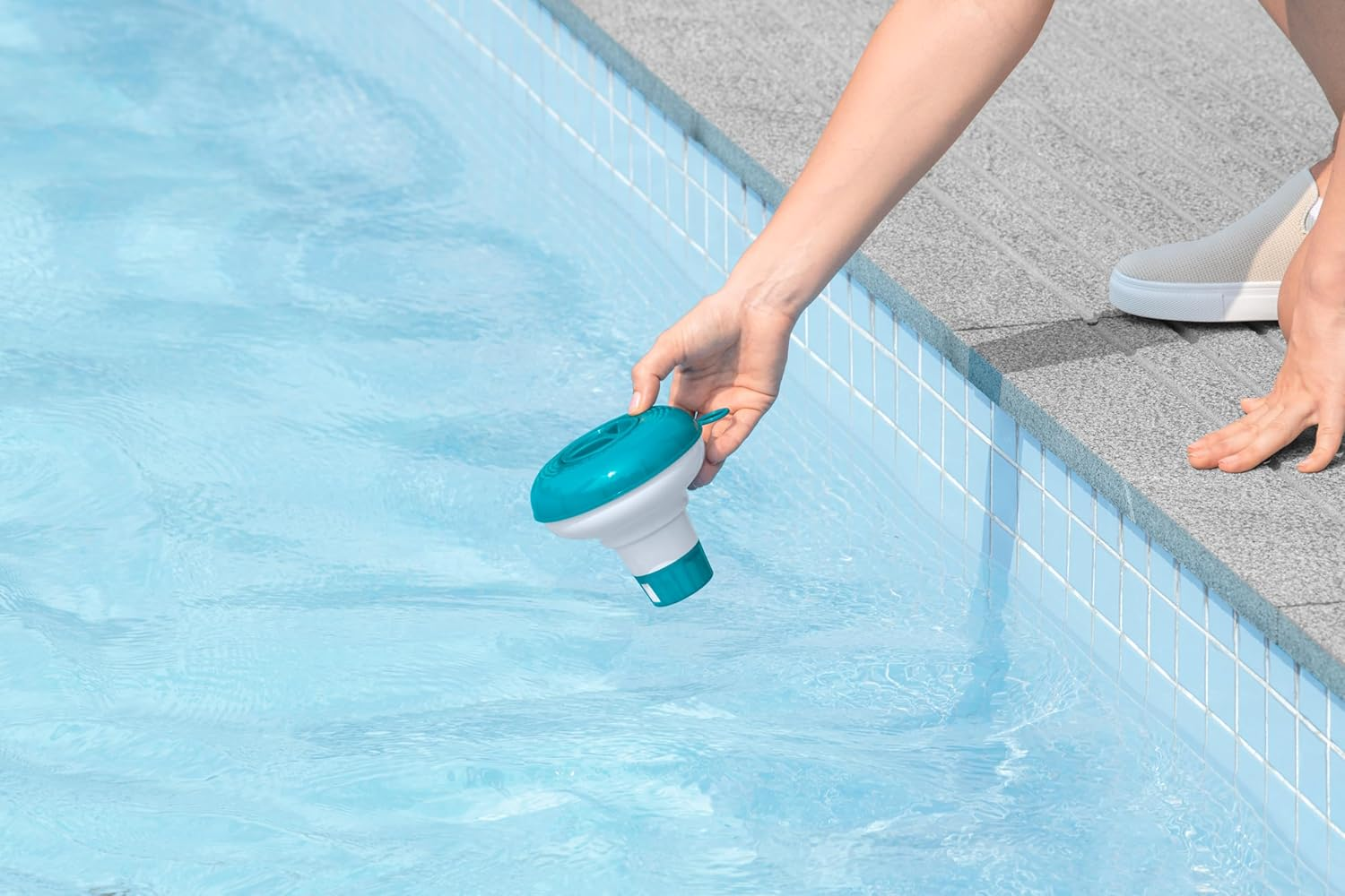 Eine Hand setzt einen blauen und weißen Tabletten-Spender in einen Pool.
