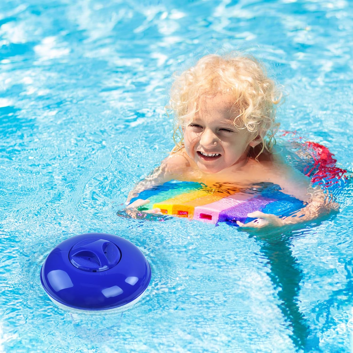 Ein Kind mit blonden Locken schwimmt im Pool mit einem bunten Schwimmbrett und einem blauen Poolschwimmer.