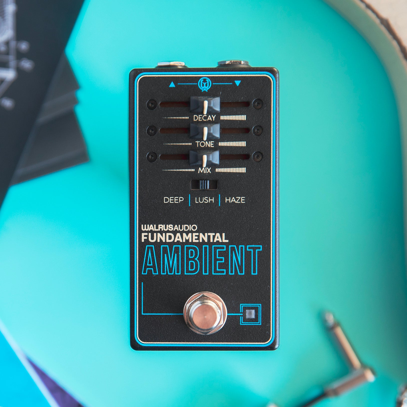 Een zwart gitaareffectpedaal met blauwe accenten op een turquoise achtergrond.