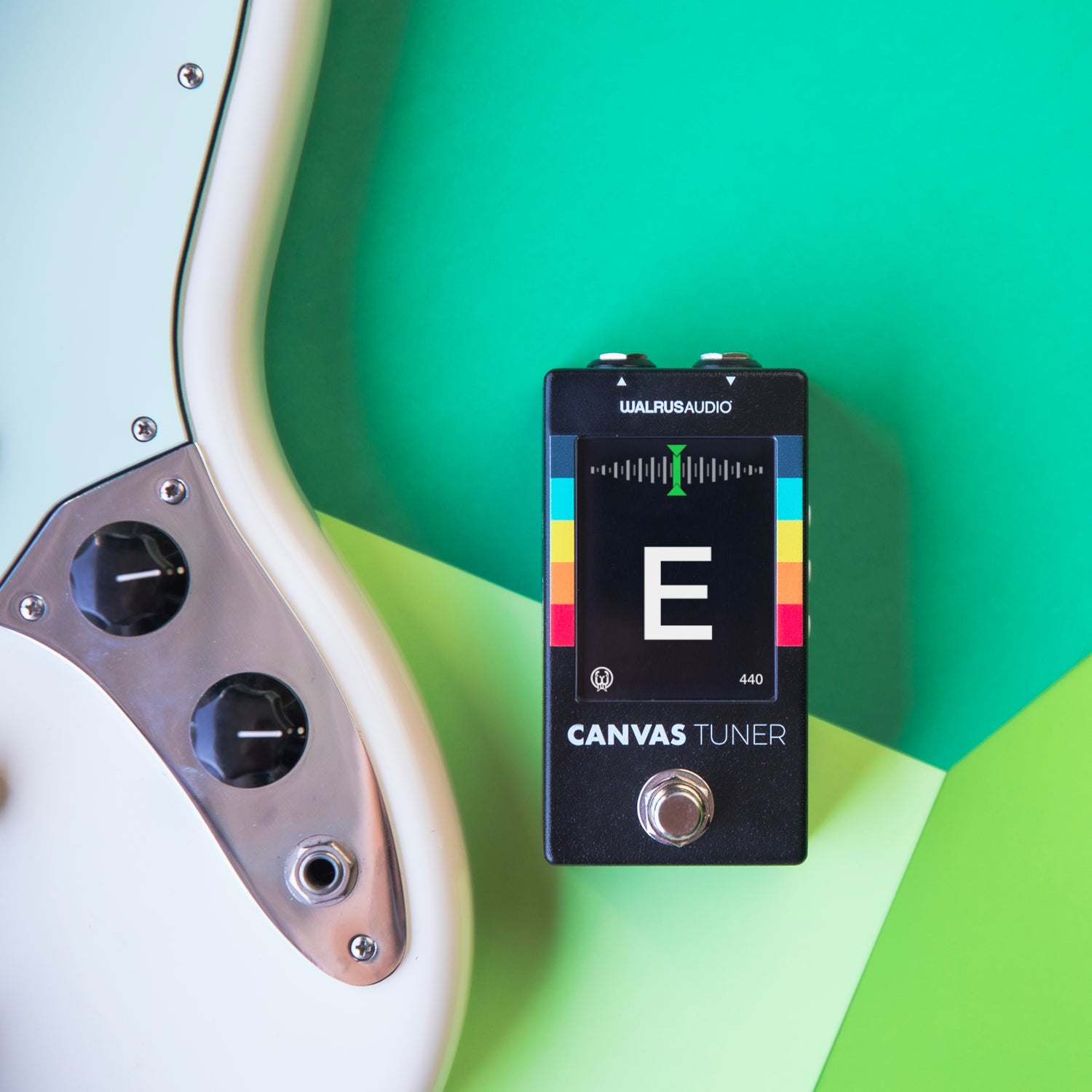 Een witte elektrische gitaar en een zwarte Walrus Audio tuner op groene achtergrond.
