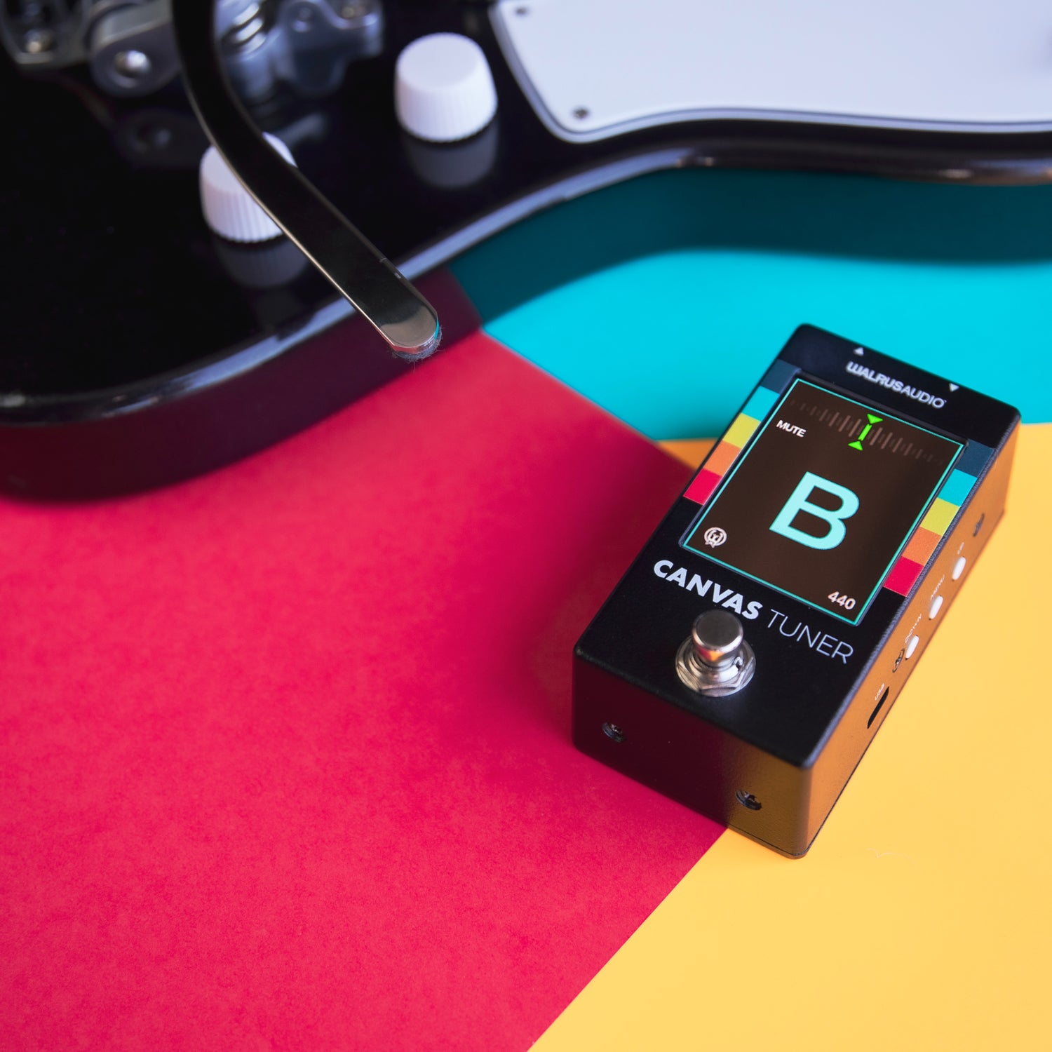 Een gitaartuner ligt naast een elektrische gitaar op kleurrijke achtergronden.