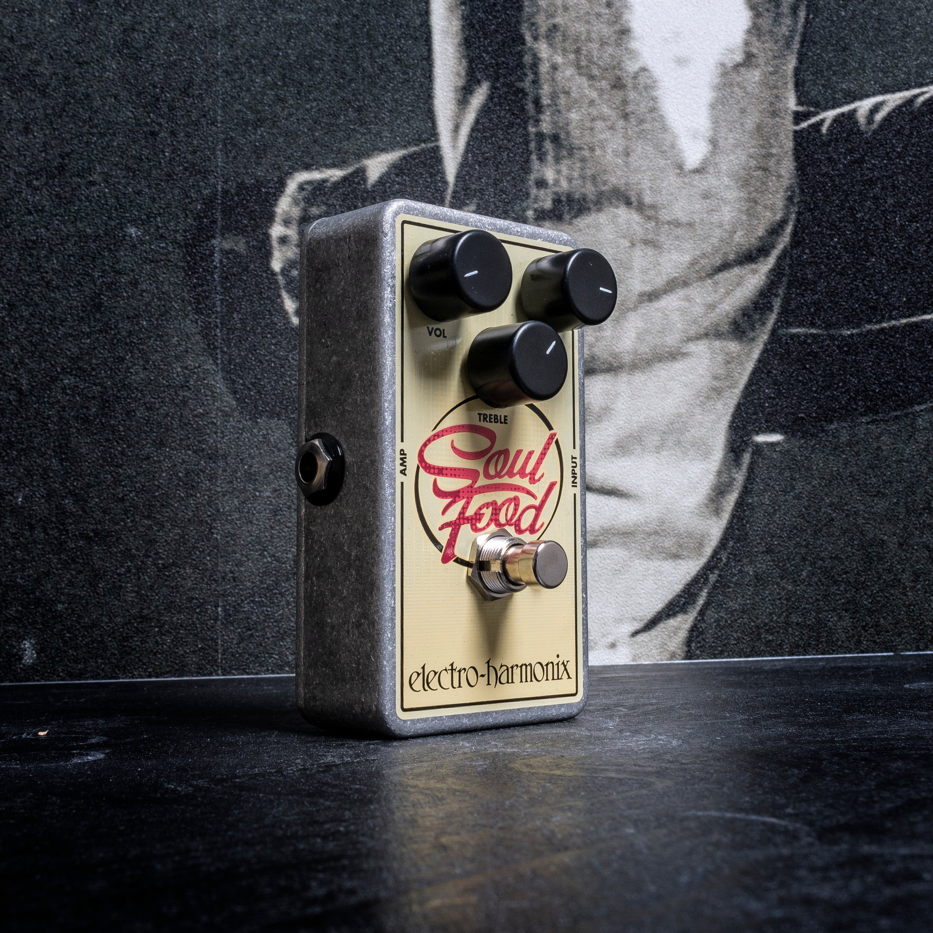 Een Electro-Harmonix Soul Food pedaal op een donker oppervlak voor een zwart-wit achtergrond.
