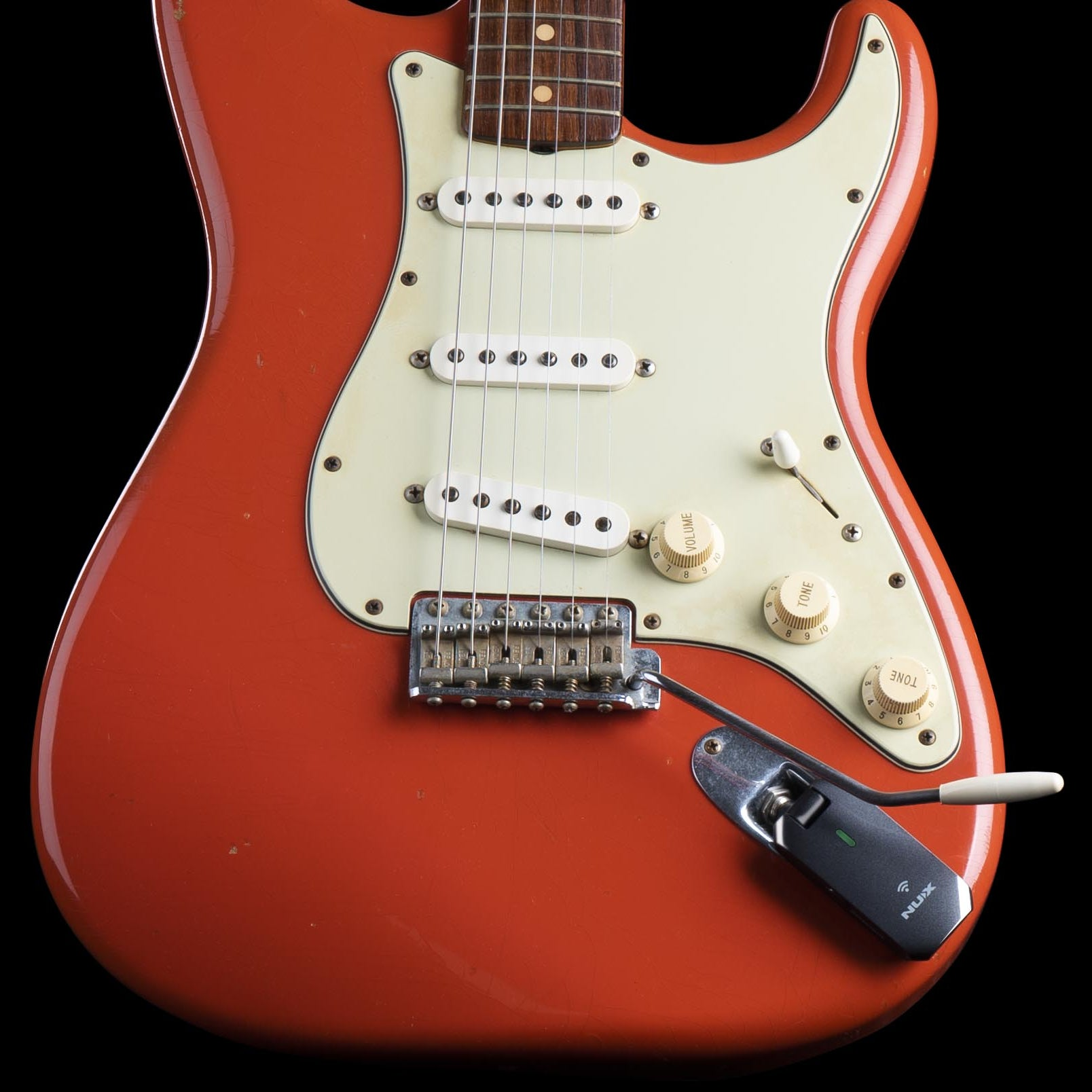Oranje elektrische gitaar met crème slagplaat, drie pickups en een NUX zender.