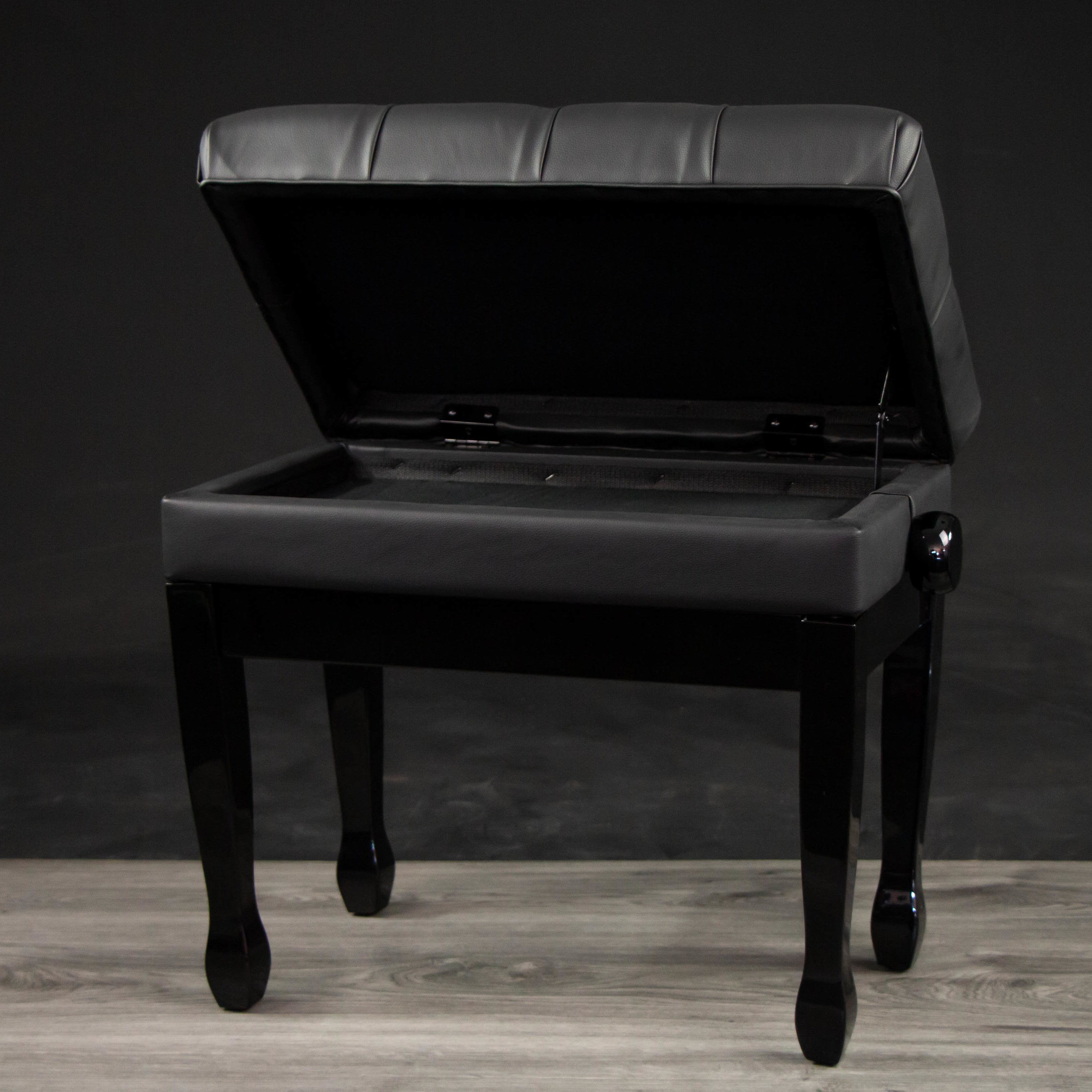 A black piano bench with its lid open, revealing storage space inside.