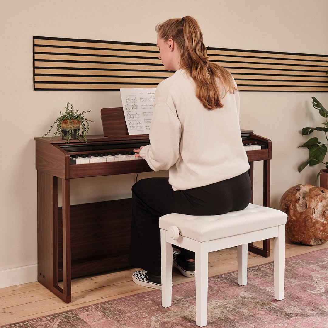 A young woman plays piano on a dark wood piano, sitting on a white bench.