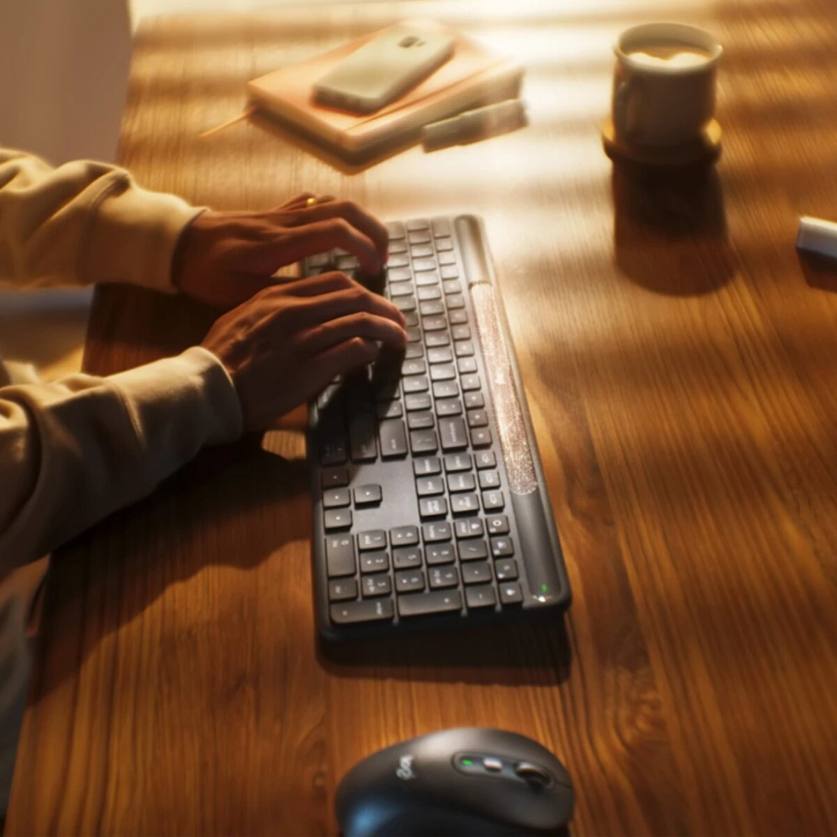 Mani che digitano su una tastiera su una scrivania di legno. Mouse, caffè e taccuino vicini.