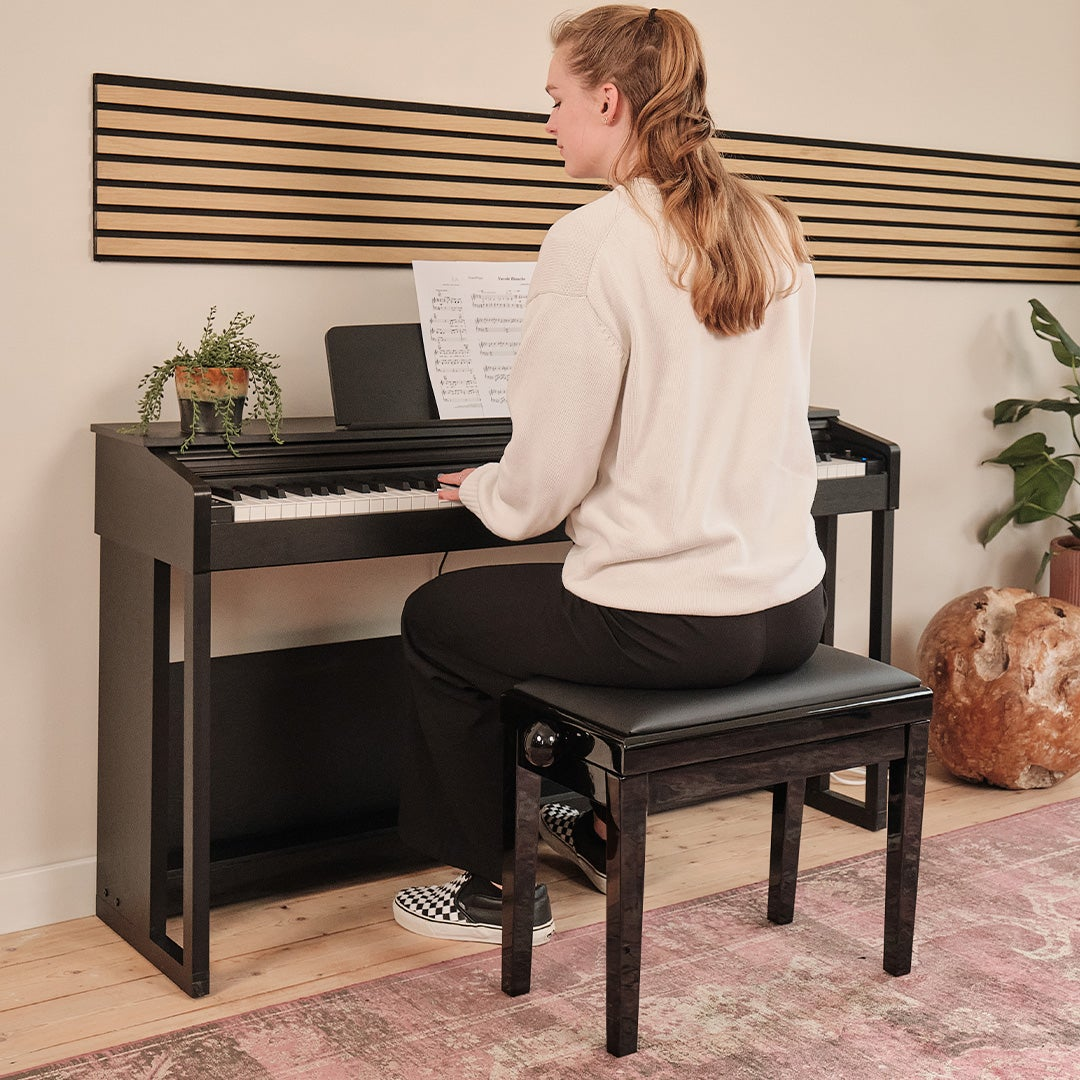 A woman with blonde hair plays piano, sheet music on stand, wood paneling in background.