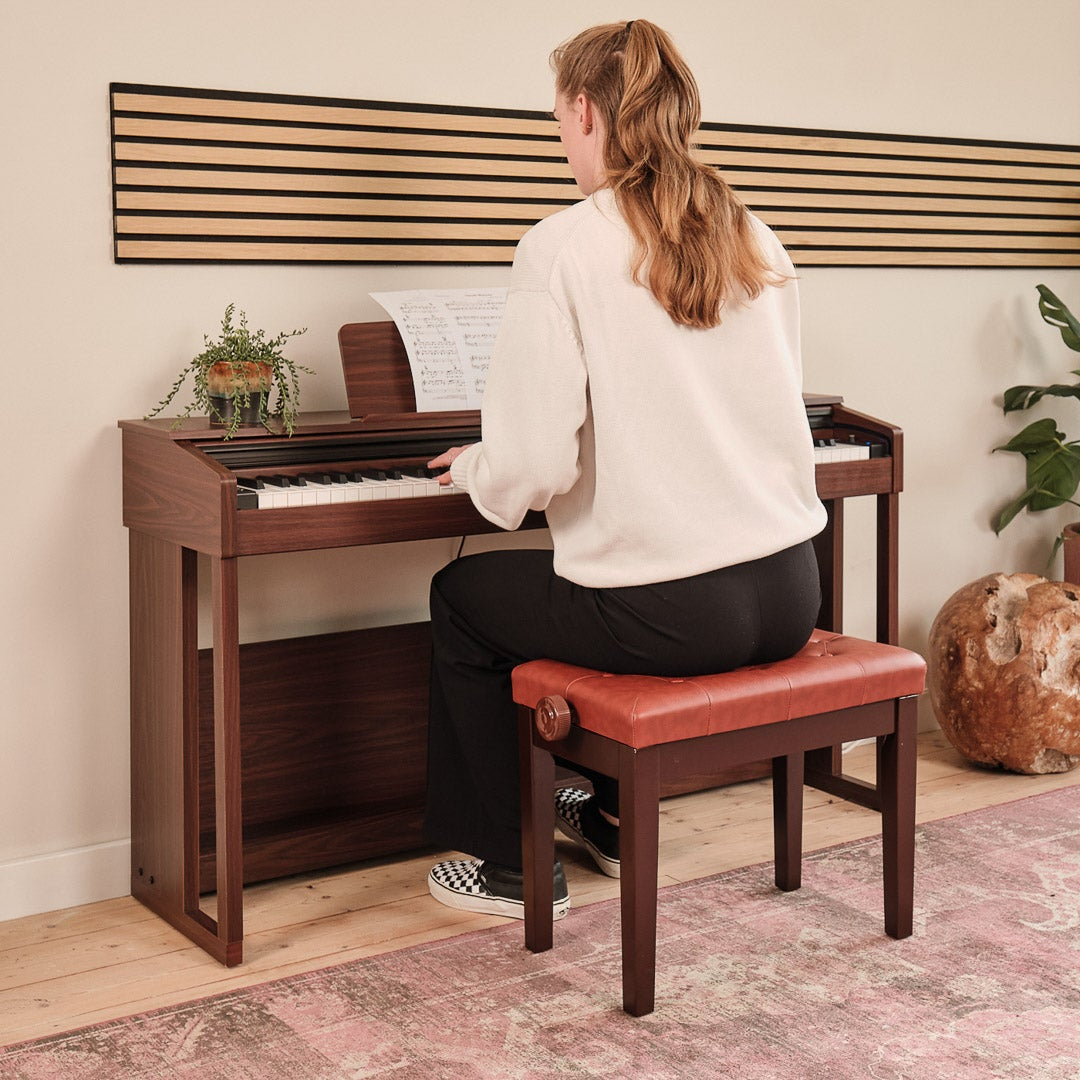 A woman plays a piano while sitting on a brown bench.