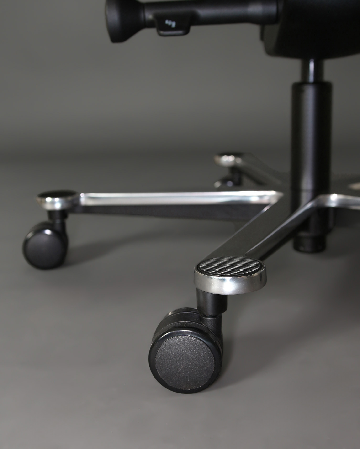 Zbliżenie czarnych kółek i metalowej podstawy krzesła biurowego na szarym tle.