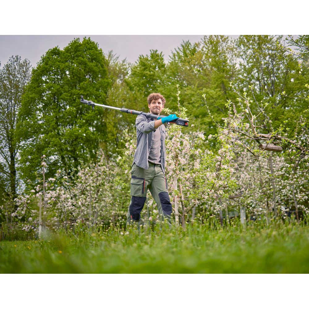 Mann im Garten trägt Astschere über der Schulter, Arbeitskleidung und Handschuhe.