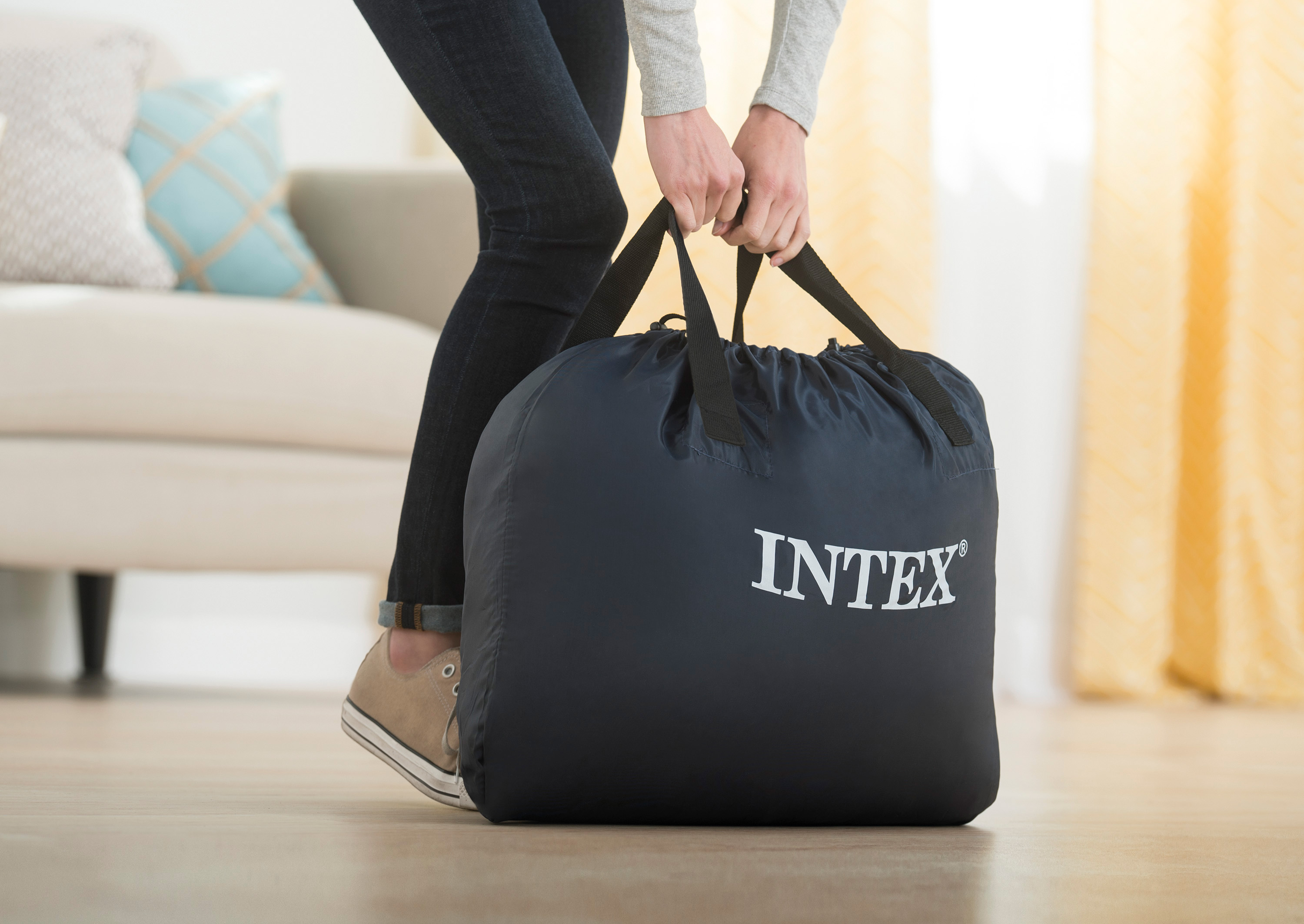 Person trägt eine dunkelblaue Intex-Tasche in einem Wohnzimmer.