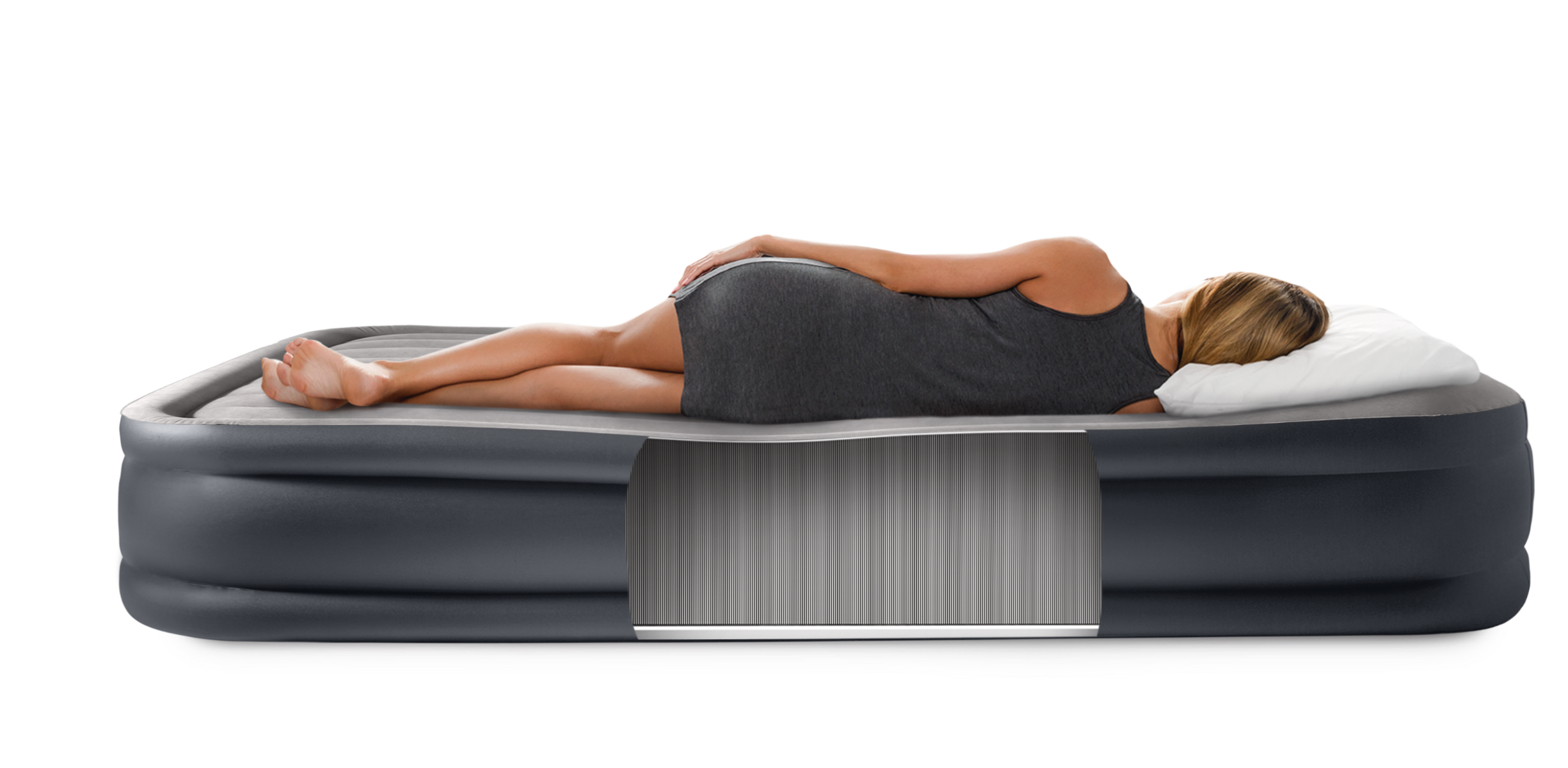 Kobieta leży na materacu dmuchanym, w szarej sukience, z białym poduszką.