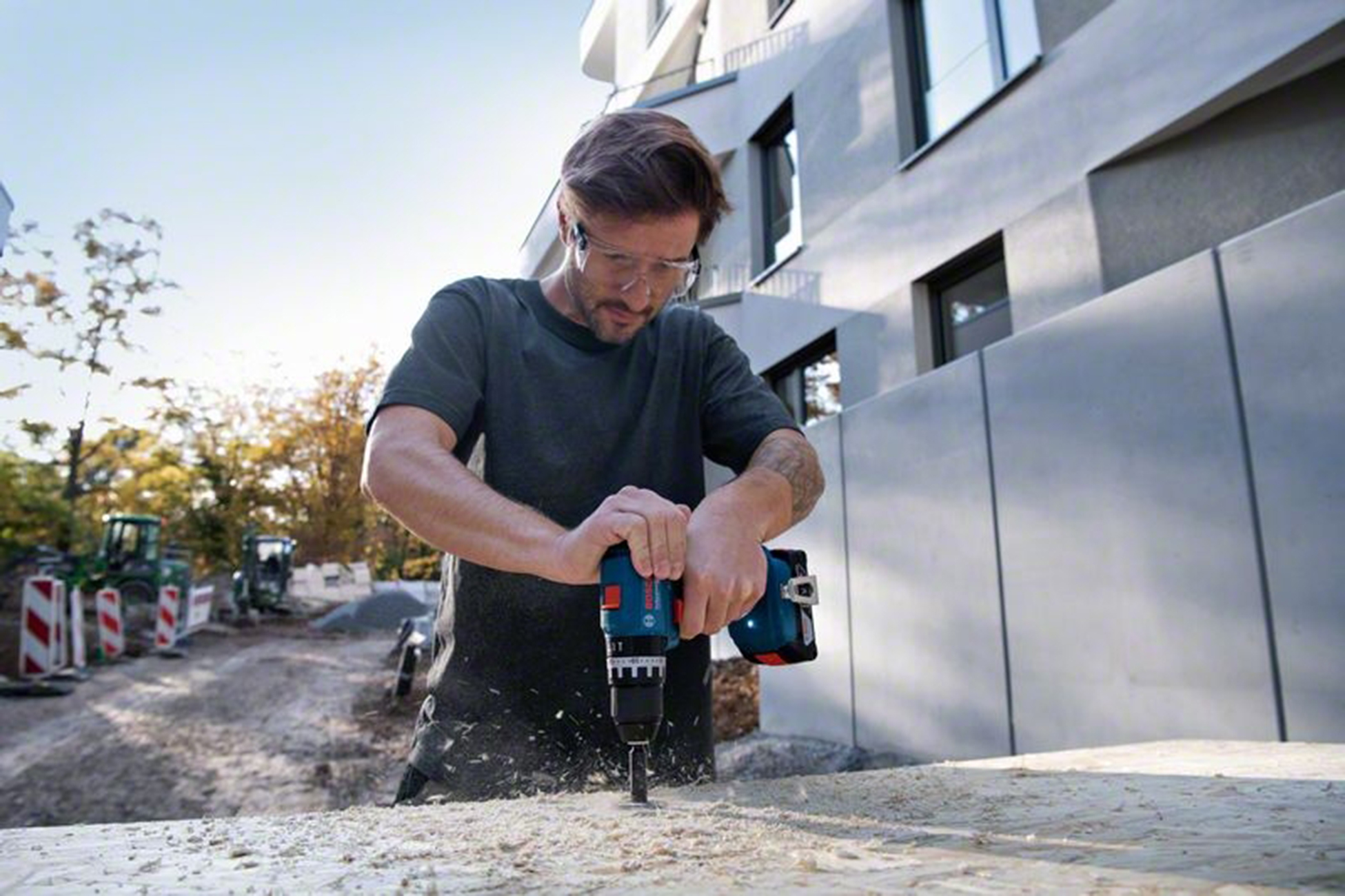 Uomo fora legno; cantiere con trattore ed edificio sullo sfondo.