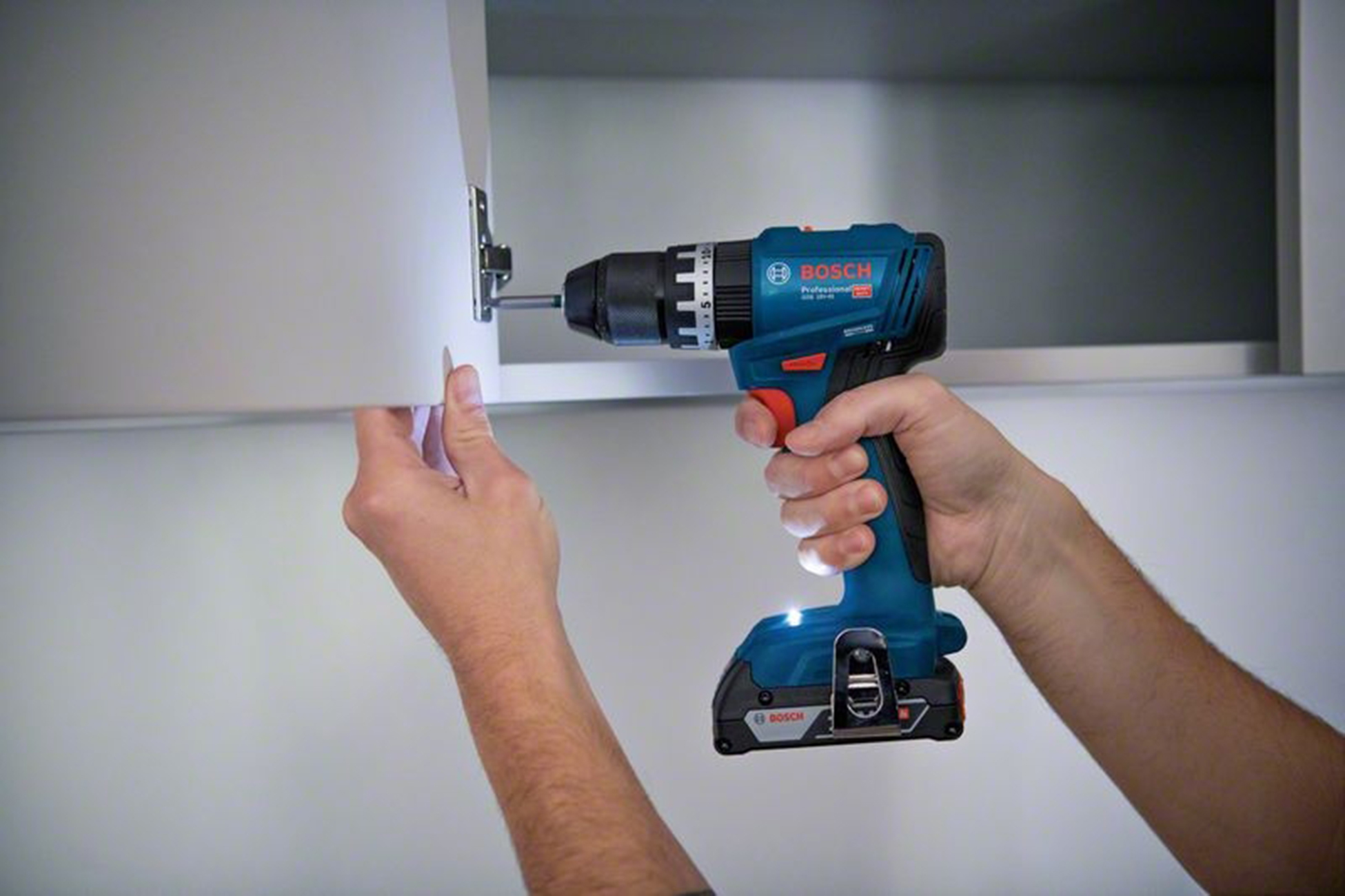 Una mano usa un trapano Bosch blu per fissare un'anta di un armadio con una vite.
