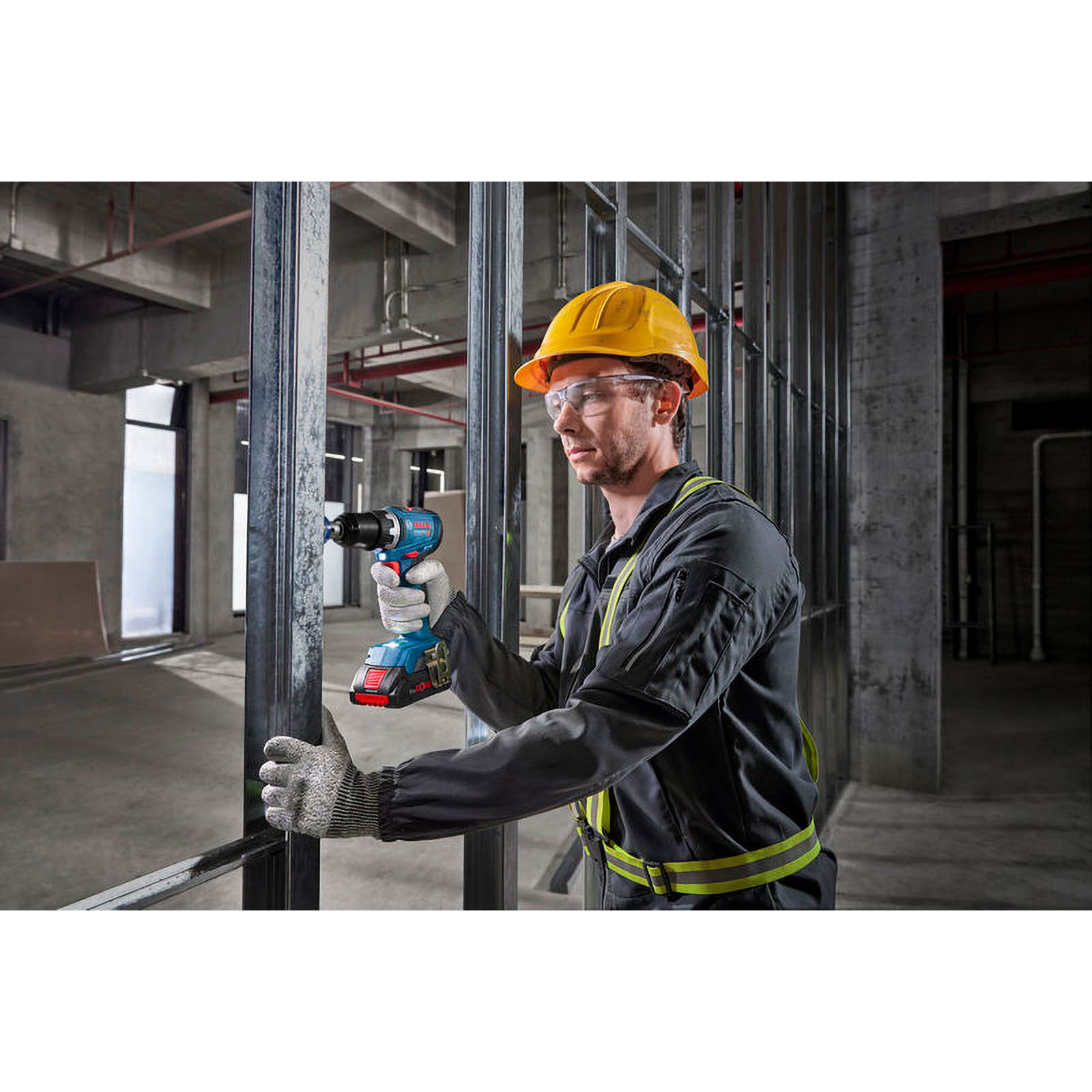Ein Mann mit Helm bohrt in einem Metallrahmen. Dunkler Arbeitsanzug, Handschuhe.