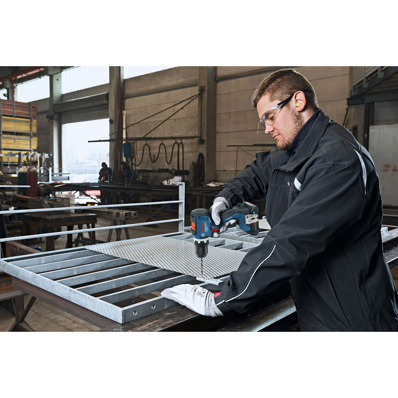 Ein Mann bohrt in einem Metallgitter in einer Werkstatt.