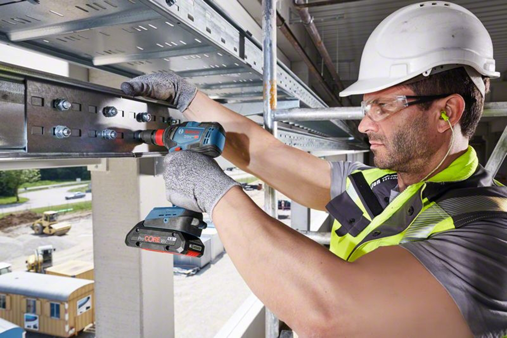 Bauarbeiter mit Helm und Warnweste bohrt Metallkonstruktion.