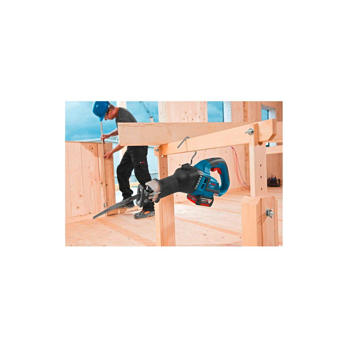 Ein Mann in einem blauen Helm arbeitet mit Holz. Eine Säge hängt an einem Balken.