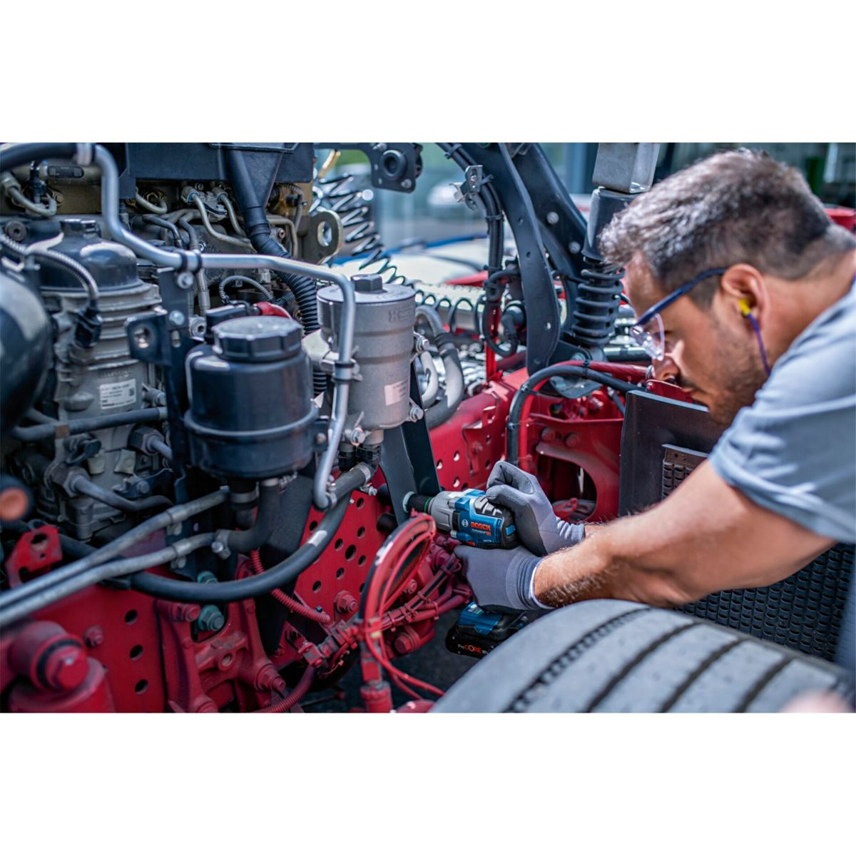 Mezczyzna w okularach i rekawiczkach pracuje przy silniku wiertarka.