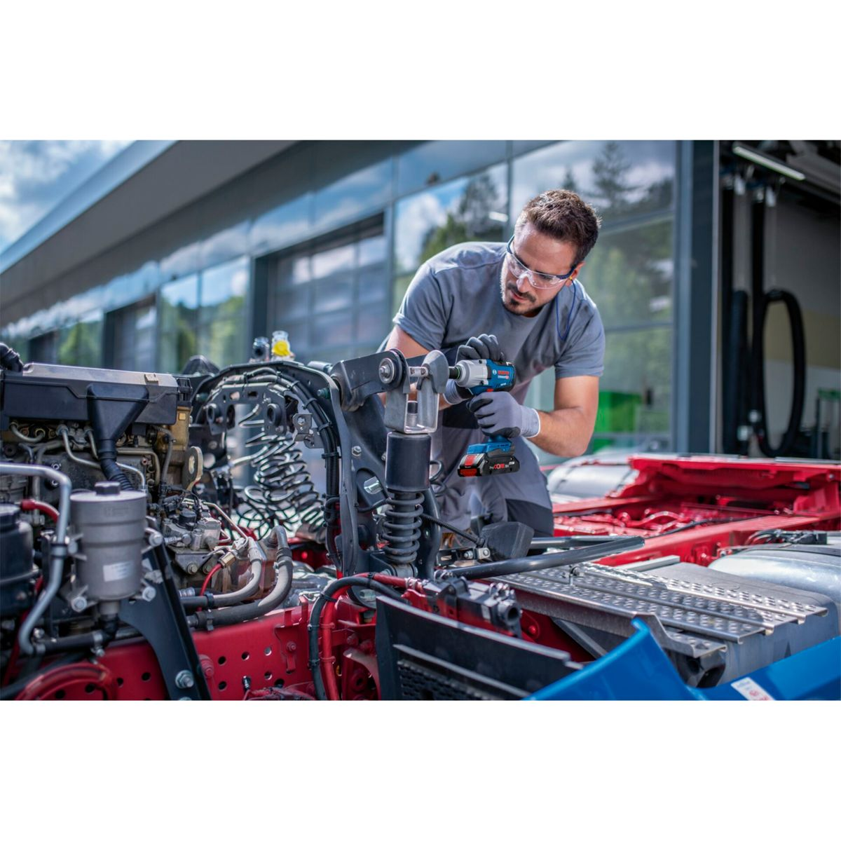 Mechanik w okularach ochronnych używa klucza udarowego akumulatorowego do silnika ciężarówki.