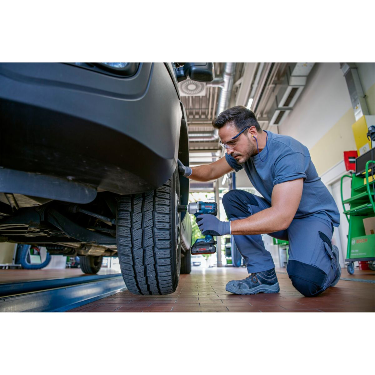 Mechanik klęczy obok samochodu, używając klucza udarowego do opony.