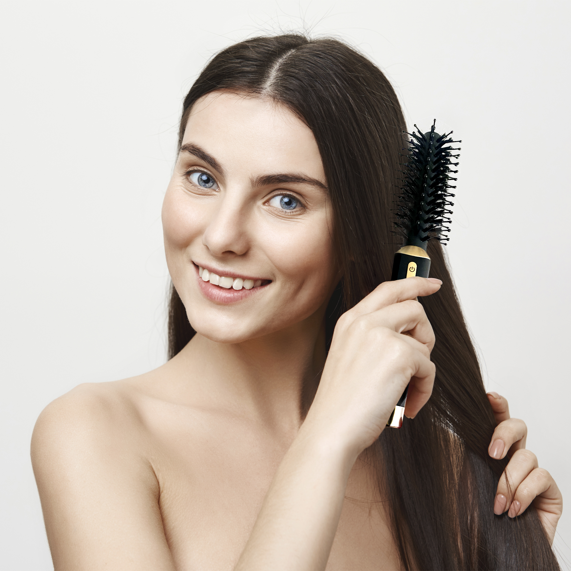 Mujer con cabello castaño cepillándose el cabello con un cepillo redondo negro.