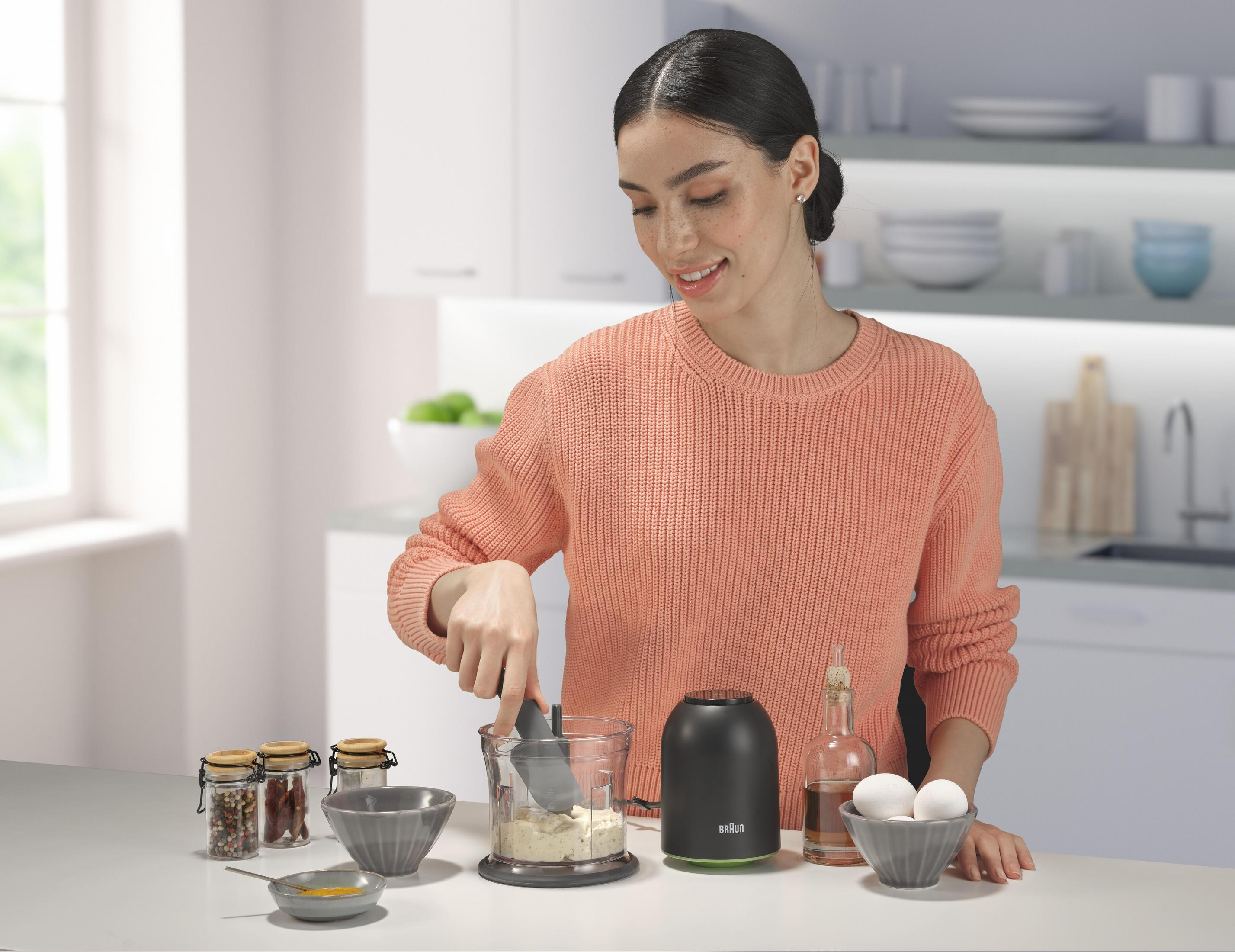 Una donna con un maglione color corallo usa un robot da cucina nero in cucina.
