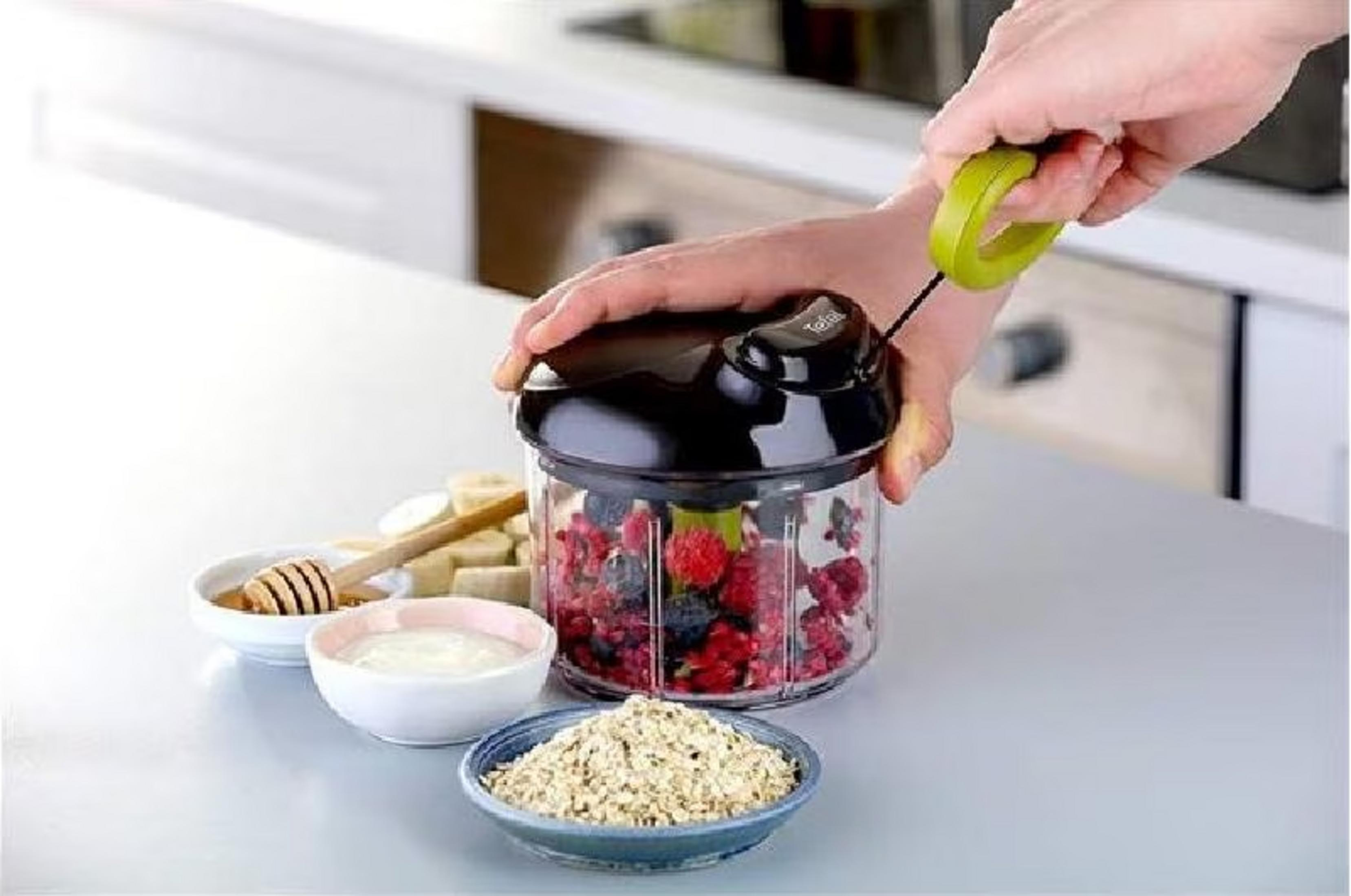 Eine Hand zieht an einem grünen Griff, um eine Küchenmaschine mit Beeren zu bedienen.