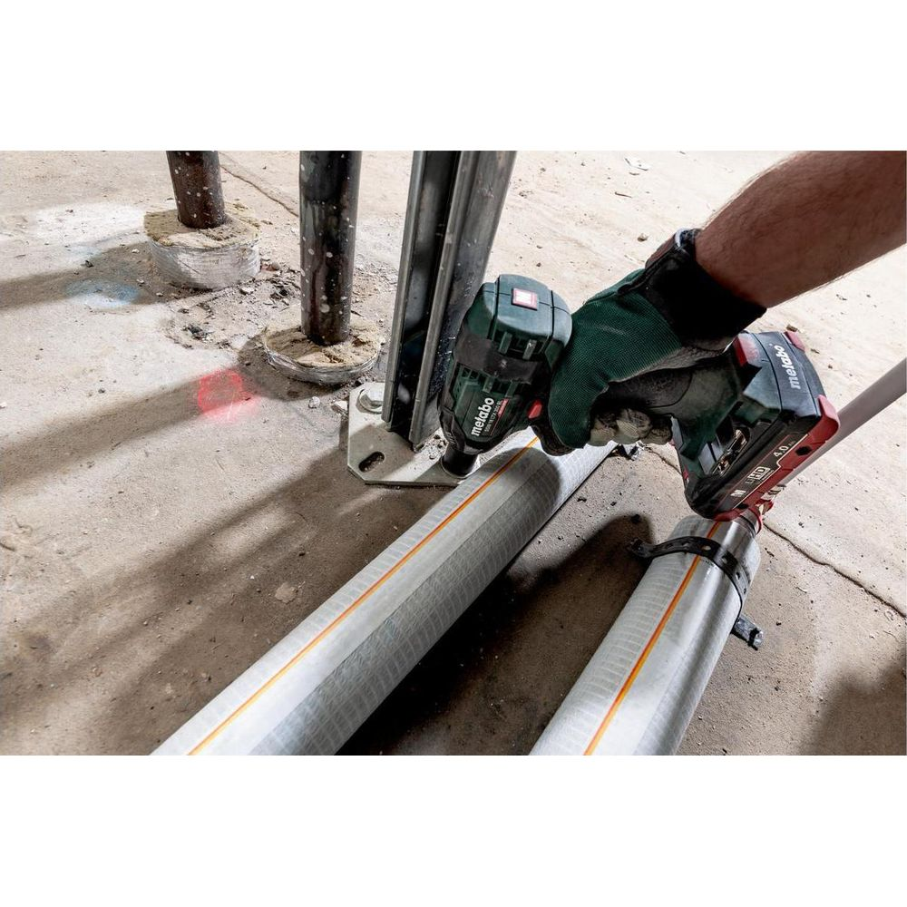 Hand mit Akkuschrauber fixiert ein Rohr an Metallstützen auf Betonboden.