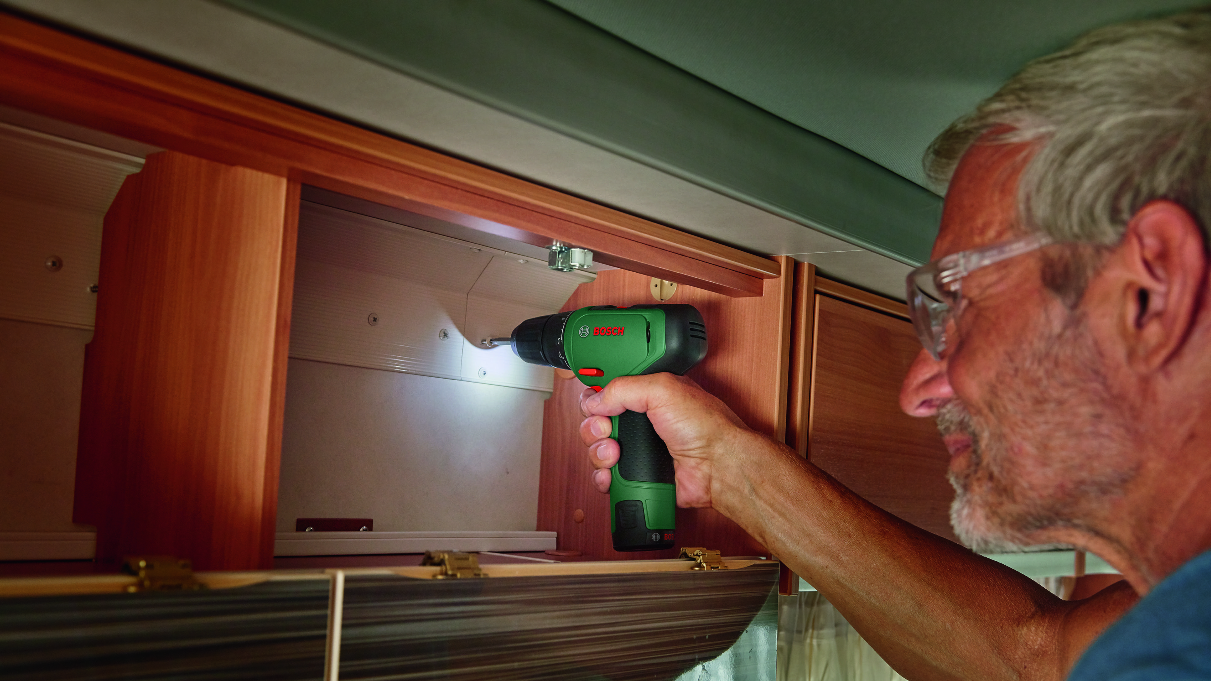 Mężczyzna używa wkrętarki akumulatorowej w szafce kampera.