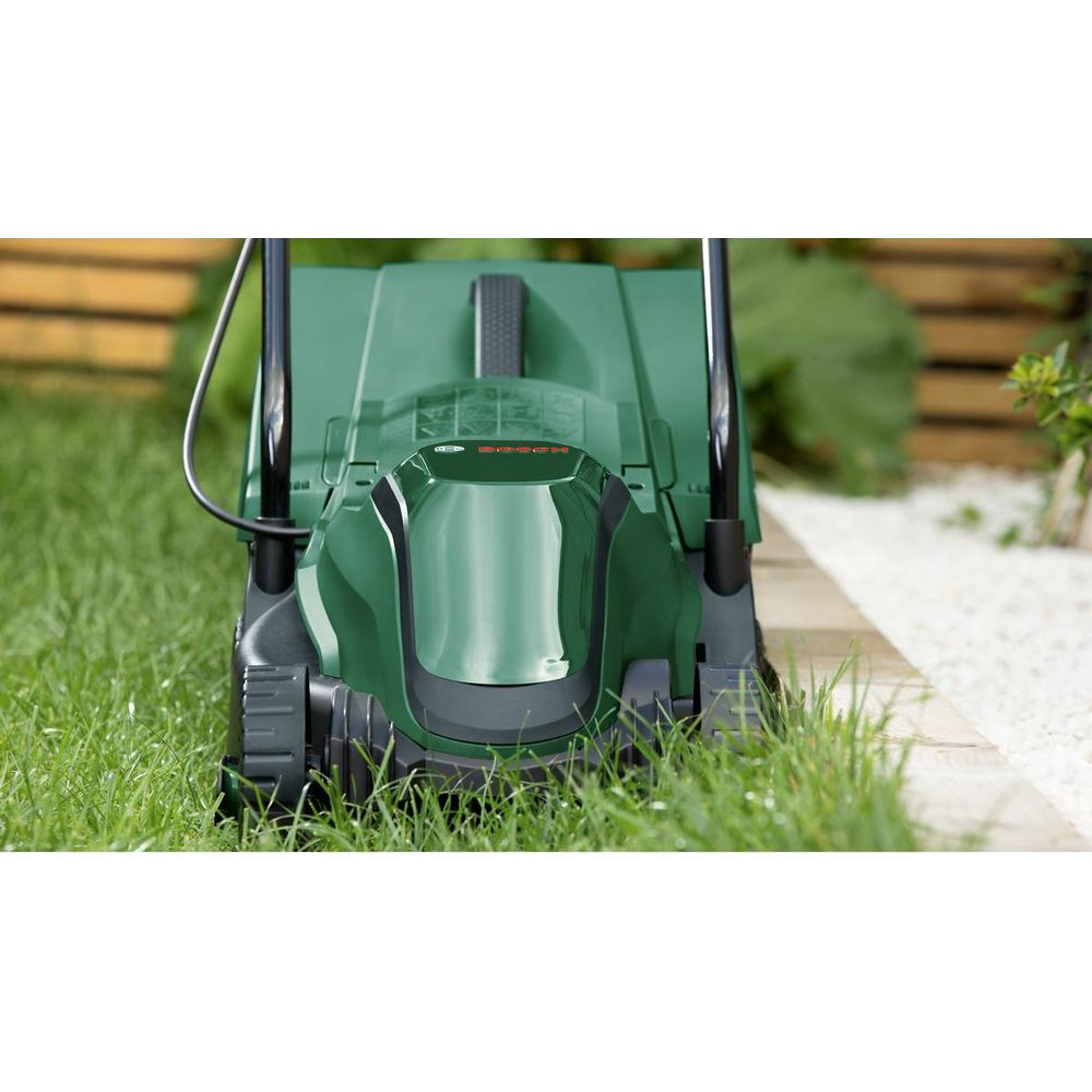 Yeşil bir Bosch çim biçme makinesi, çakıllı bir yolun yanında çimlerde duruyor.