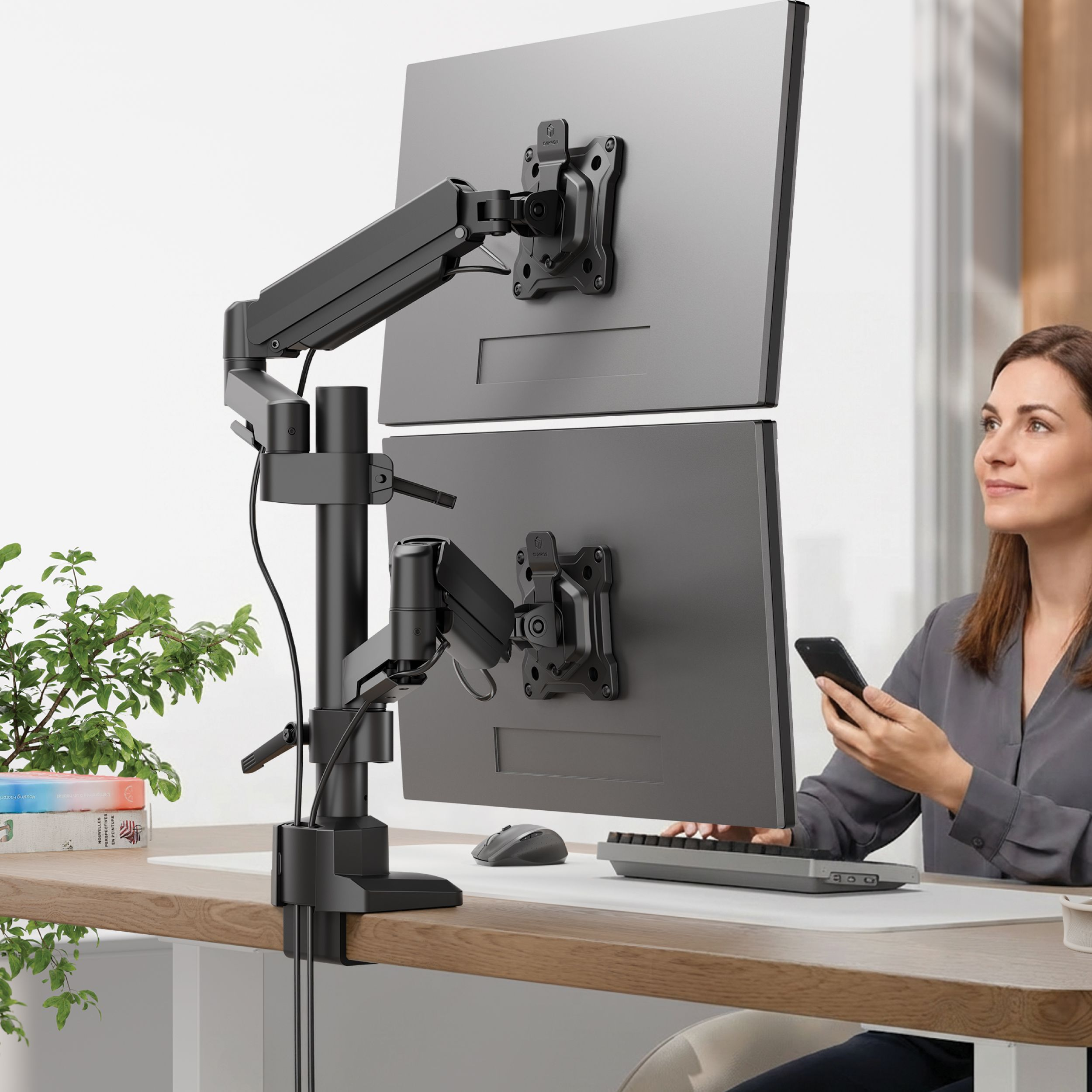 Kobieta ze smartfonem siedzi przy biurku z dwoma monitorami na ramieniu.