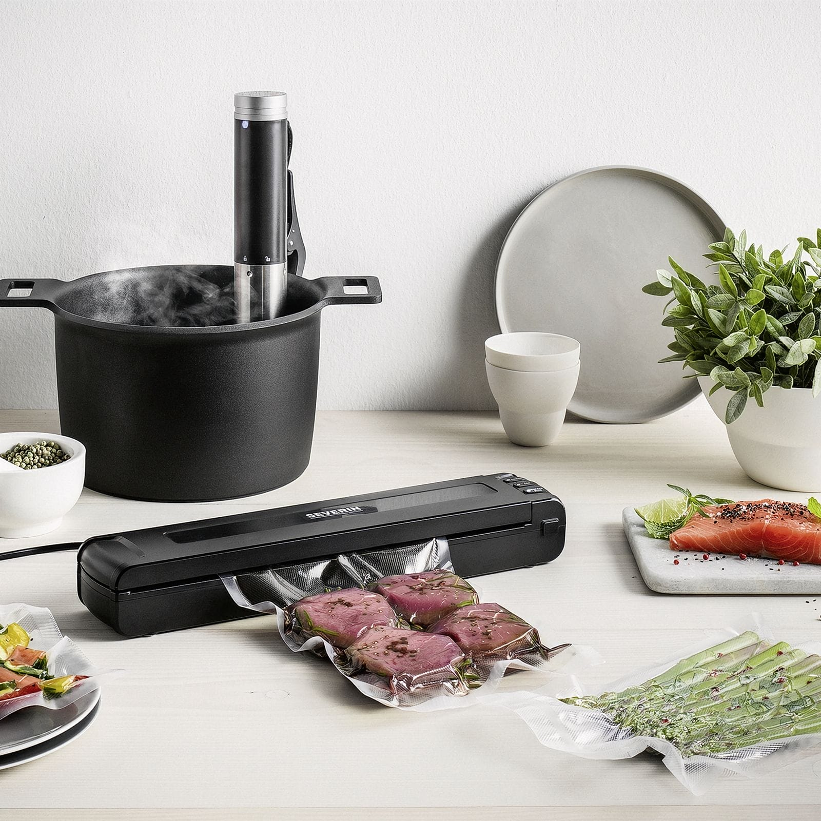 Sous-vide-Garer in Topf, Vakuumierer mit Fleisch, Lachs und Spargel.