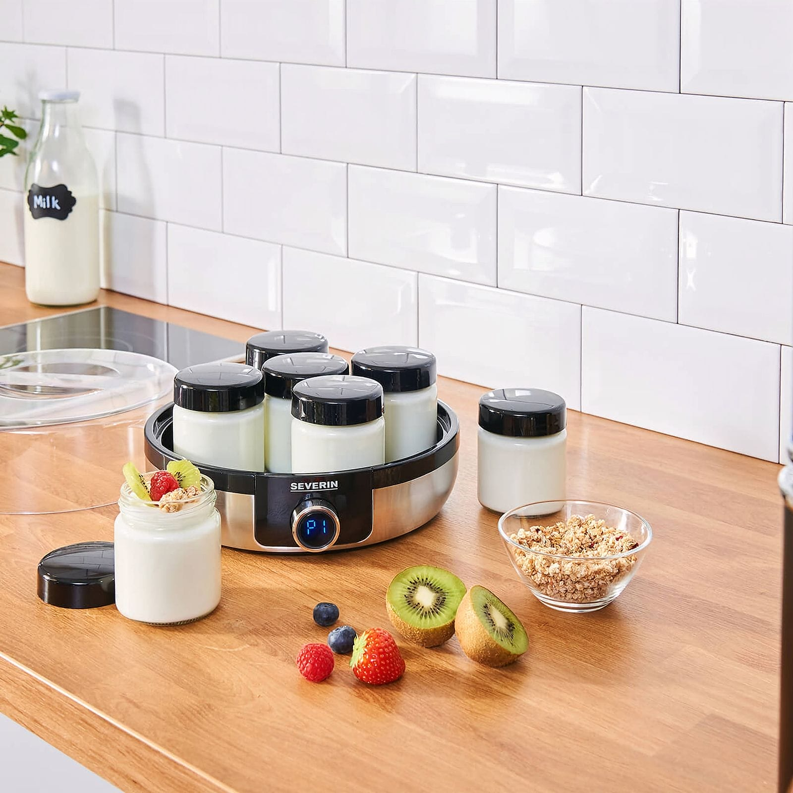 Máquina de yogur con frascos, frutas y muesli en un mostrador de madera.