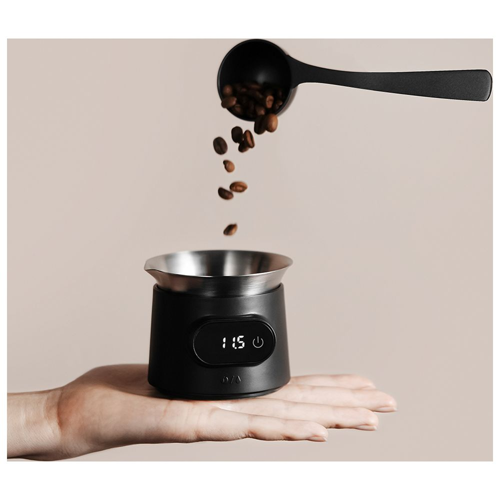 Chicchi di caffè cadono da un misurino in una bilancia nera tenuta in mano.