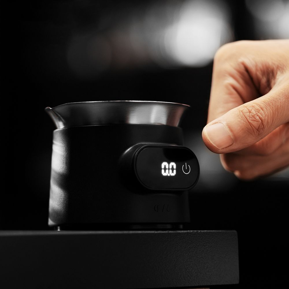 Un dito preme un pulsante su una bilancia digitale nera con display 0,0.