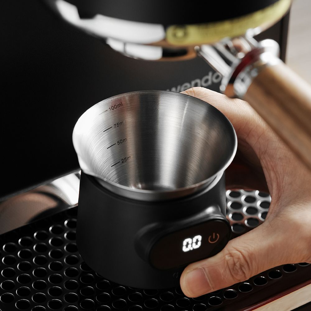 Una mano tiene una tazza in acciaio inox con segni in ml su una bilancia digitale.