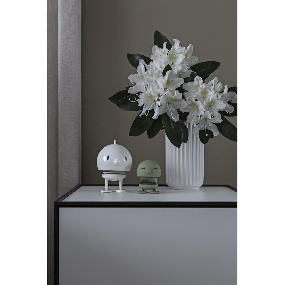 Due figure decorative, un robot bianco, uno verde, siedono su una mensola accanto a fiori bianchi.