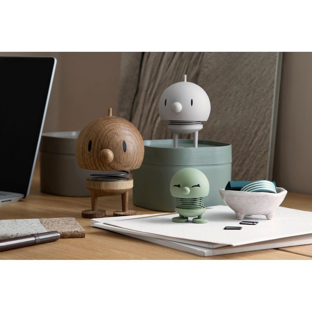 Tre figure decorative su una scrivania: una in legno, una bianca e una verde.