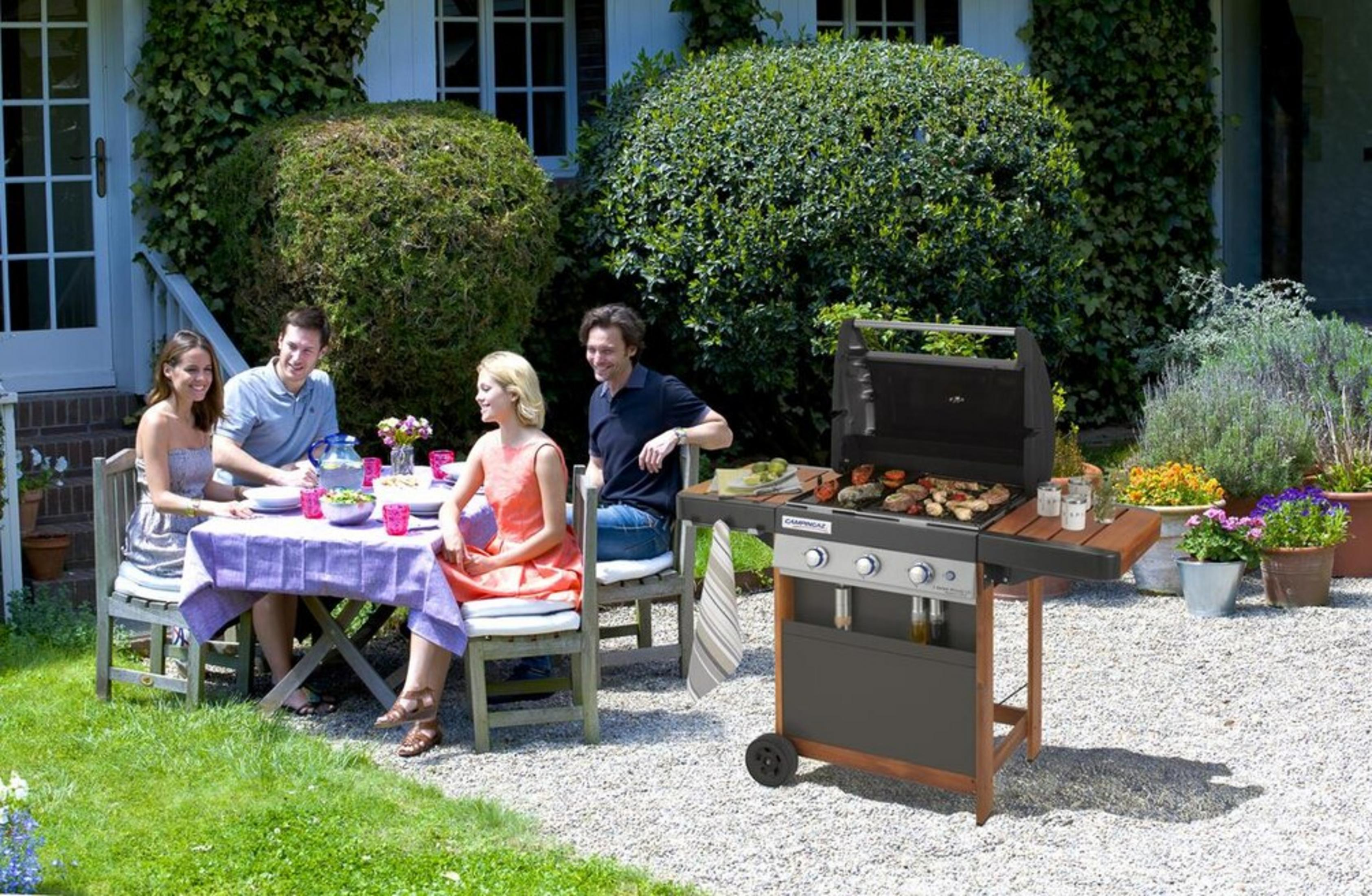 Vier Personen sitzen an einem Tisch im Garten, während ein Grill in der Nähe steht.