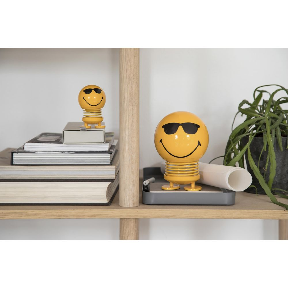 Due figure gialle di smiley con occhiali da sole su uno scaffale.