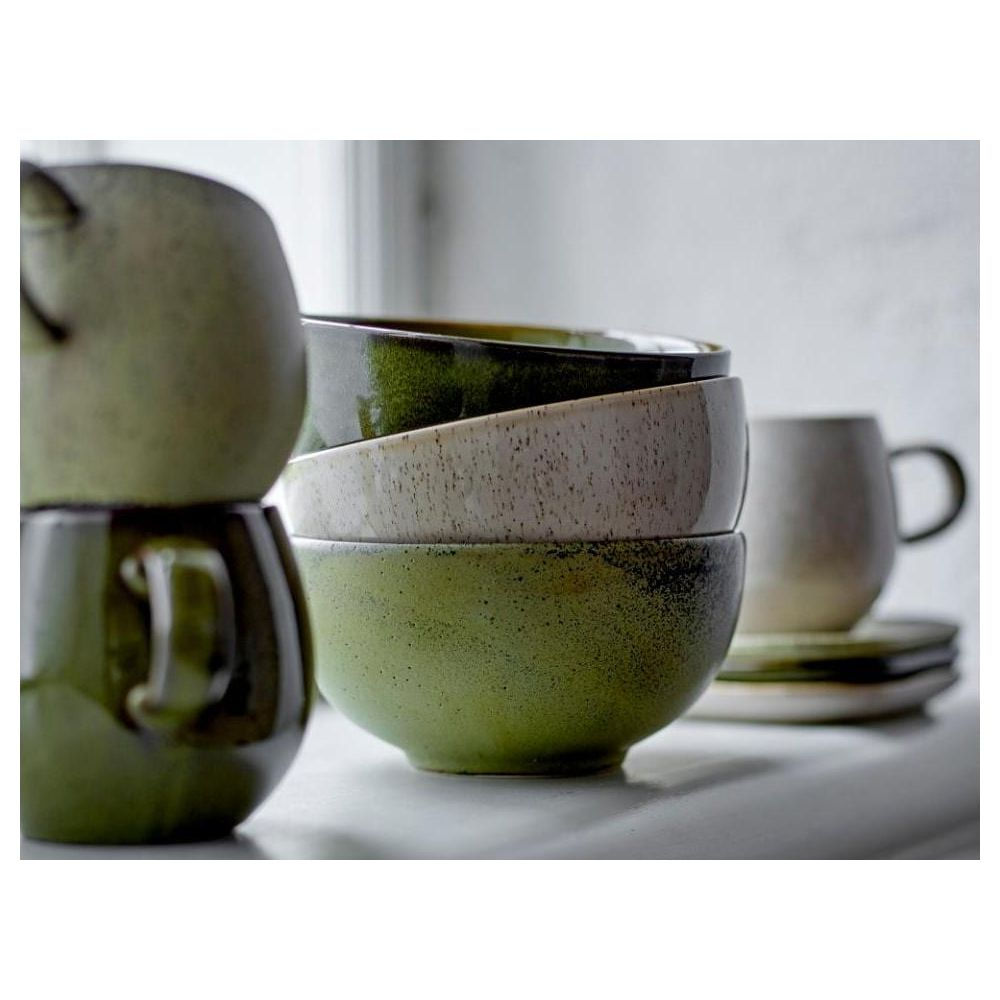 Grüne und cremefarbene Keramikschalen und eine Tasse auf einem Regal.