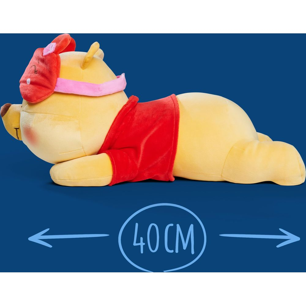 Peluche Winnie the Pooh giallo con maschera da notte e maglietta rossa su sfondo blu.