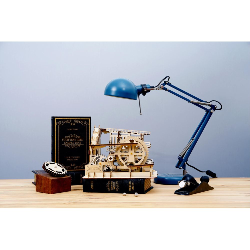 Ein Holzmodell einer Maschine steht auf Büchern neben einer blauen Lampe.
