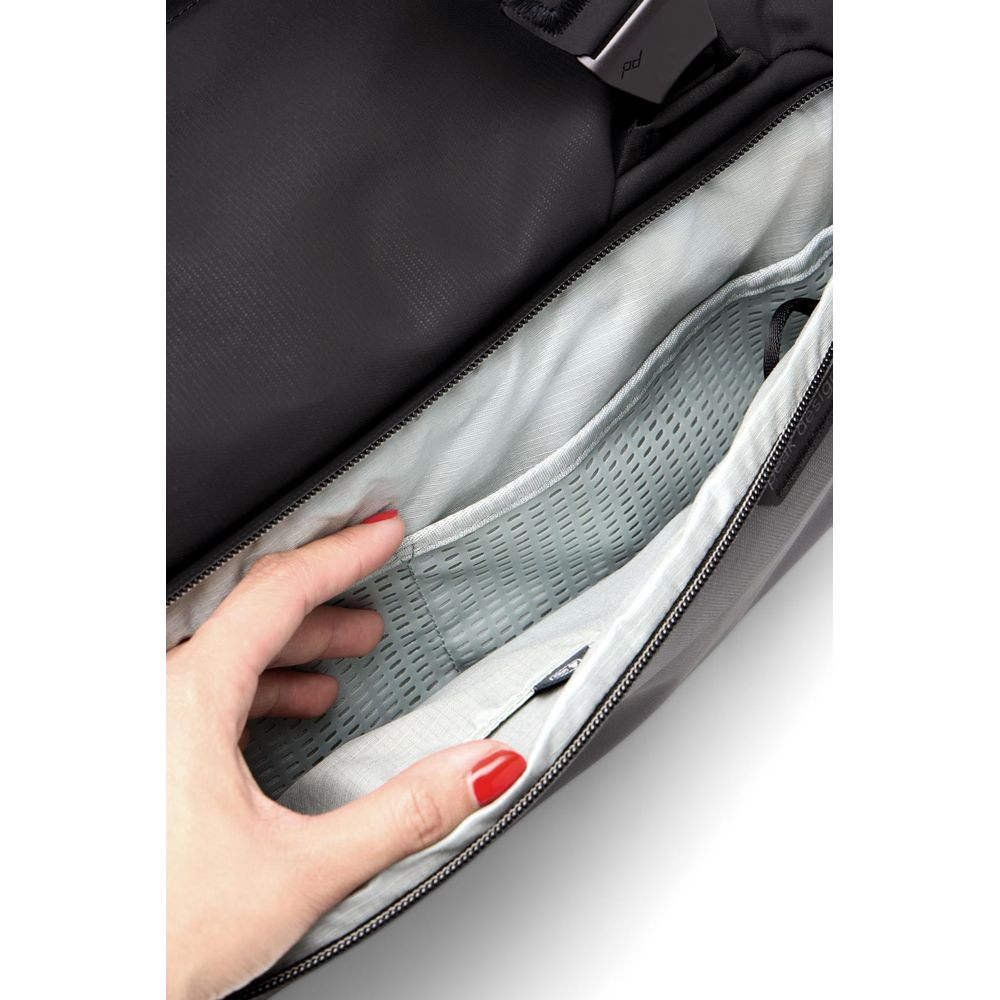 A hand with red nails reaches into a gray bag with a mesh compartment.