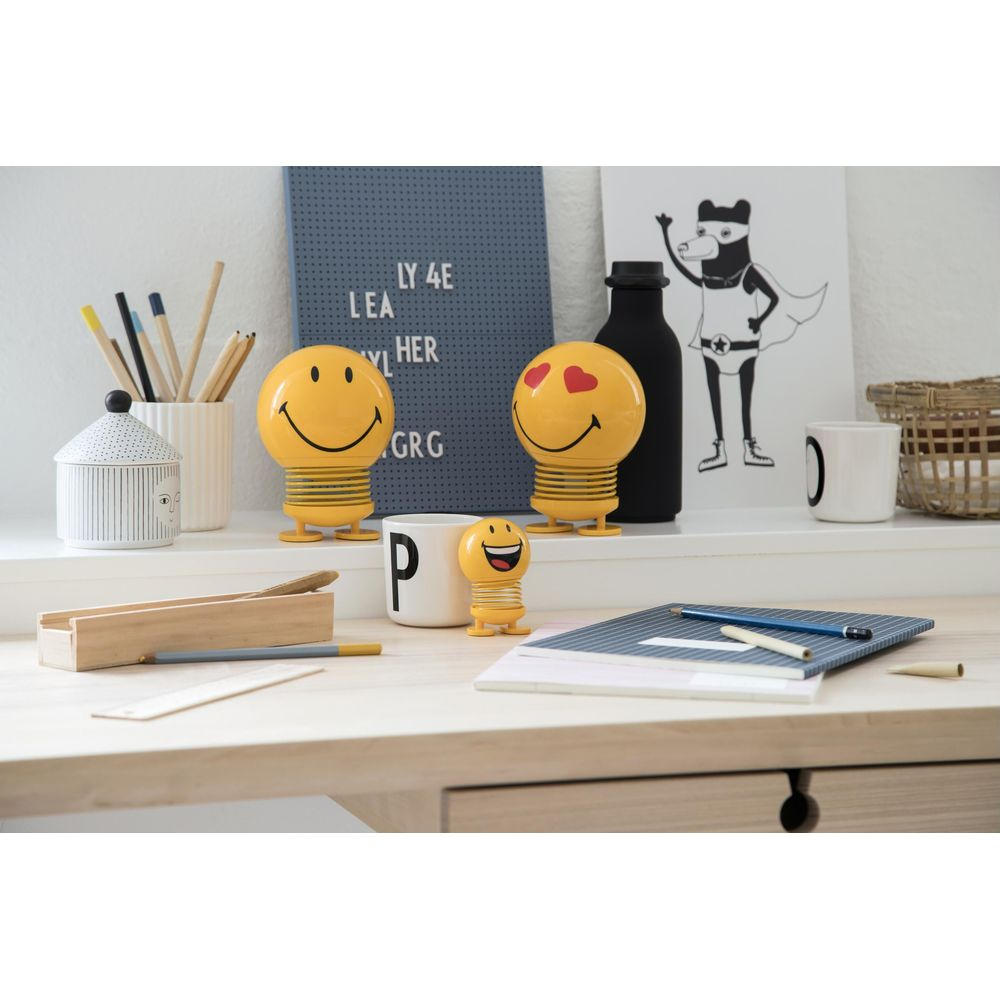 Schreibtisch mit Smiley-Figuren, Stiften, Notizbuch und Dekoration.