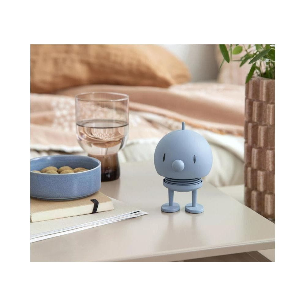 Ein blauer Roboter steht auf einem Tisch neben einer Schale mit Nüssen und einem Glas Wasser.